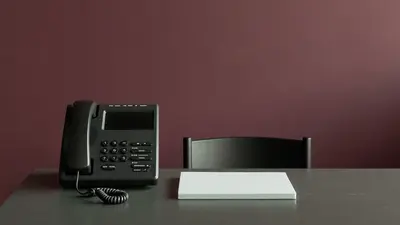 Telefono fisso nero e quaderno chiuso su una scrivania minimale
